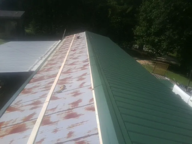 Old rusted panels beside newly installed green metal roofing — Wind Damage Roof Repair by Roofing Brothers in Connelly Springs