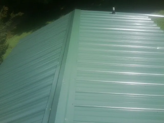 New green metal panels meeting at the ridge of a roof — Flat Roof Repair work by our crew in Connelly Springs