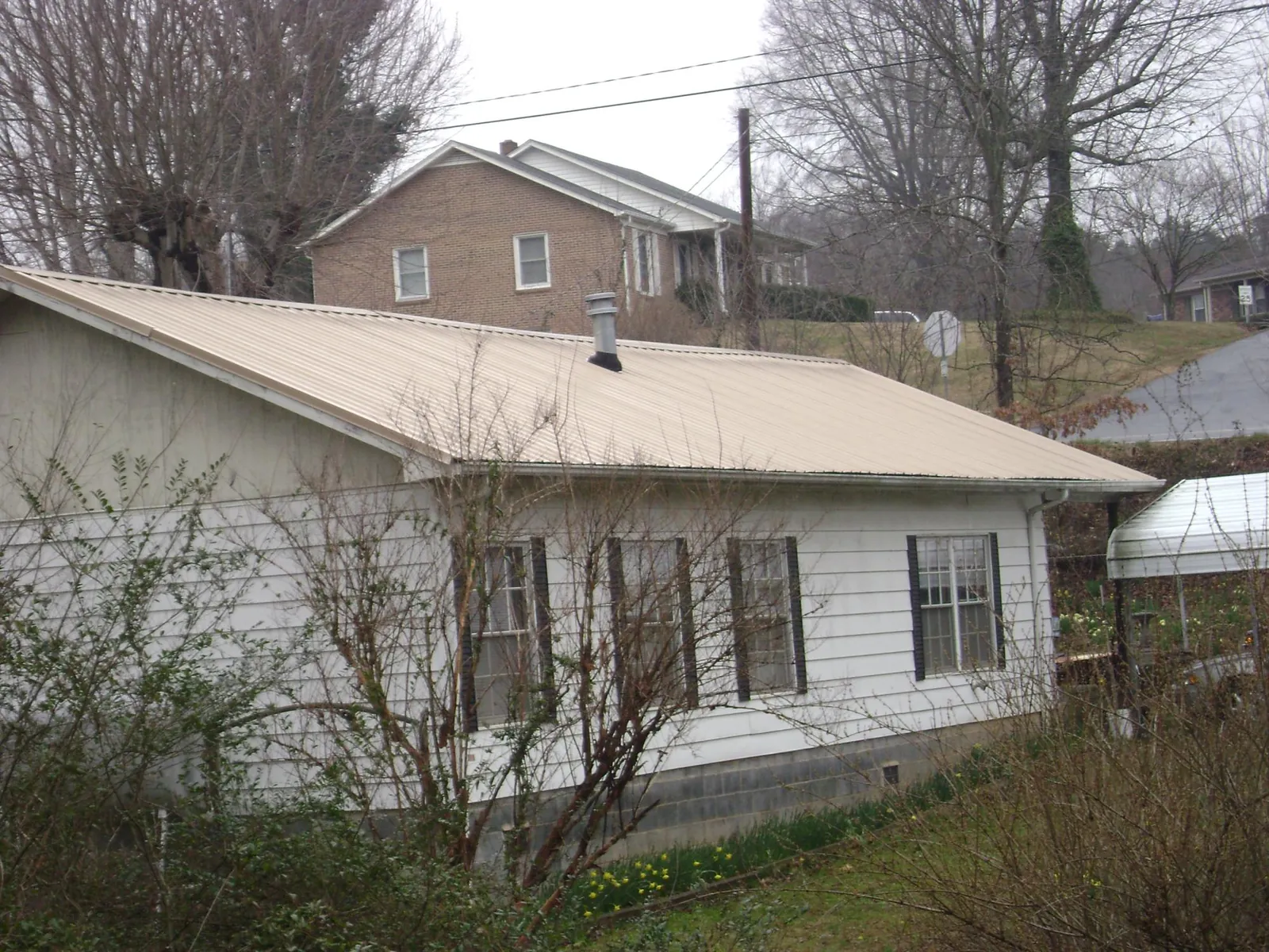Tan metal roof on a white sided house set into a hillside — Commercial Roofing by Roofing Brothers in Connelly Springs